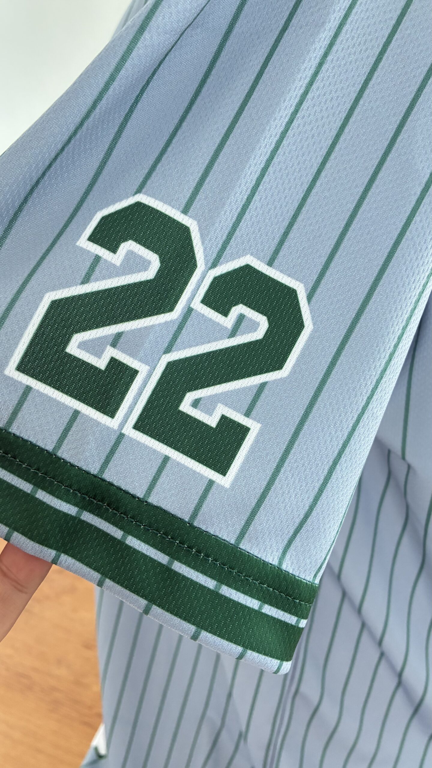 ผู้หญิงใส่เสื้อเบสบอล DRYTECH CUSTOMS HERITAGE 22 สีเทา oversize ยืนพิงผนังปูน โชว์เสื้อทีมผ้า DryTech