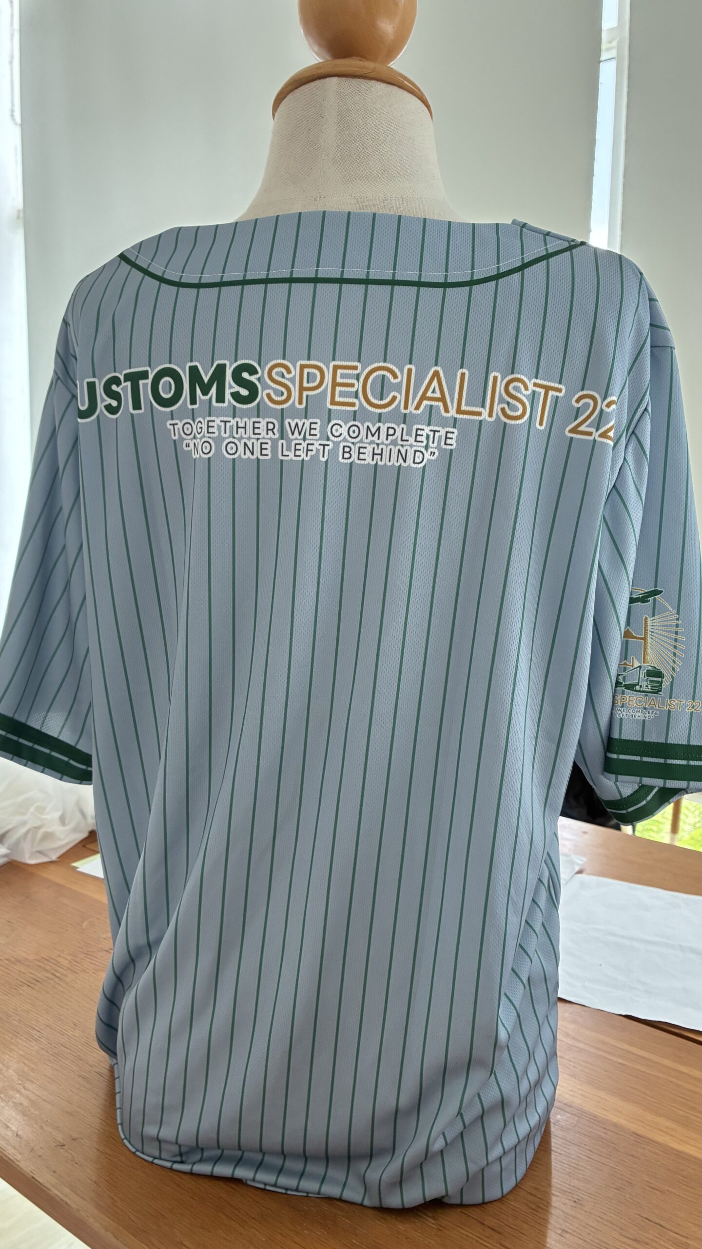 ผู้หญิงใส่เสื้อเบสบอล DRYTECH CUSTOMS HERITAGE 22 สีเทา oversize ยืนพิงผนังปูน โชว์เสื้อทีมผ้า DryTech