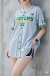 ผู้หญิงใส่เสื้อเบสบอล DRYTECH CUSTOMS HERITAGE 22 สีเทา oversize ยืนพิงผนังปูน โชว์เสื้อทีมผ้า DryTech